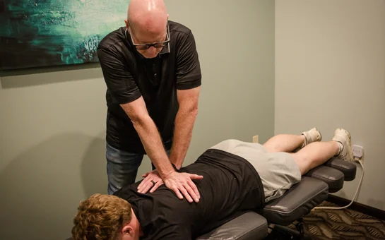 Chiropractor performing a back adjustment on a patient lying face down on a treatment table.
