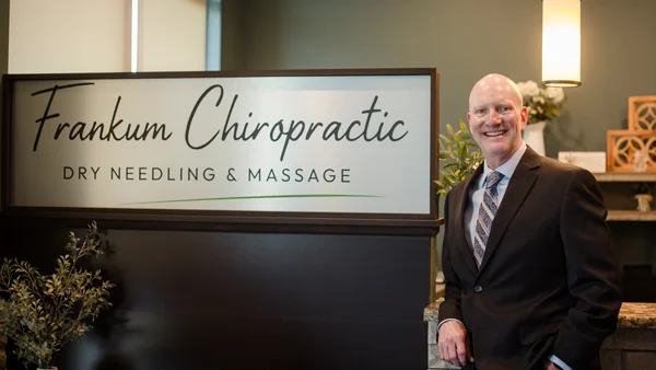 Josh Frankum standing beside the Frankum Chiropractic Dry Needling & Massage sign.